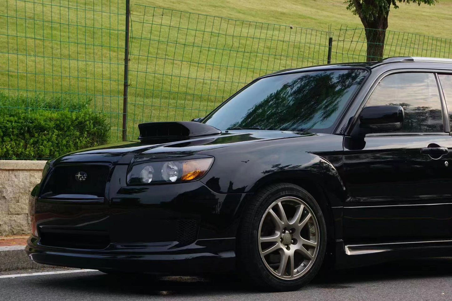 Black car parked on a street with grass and a fence in the background